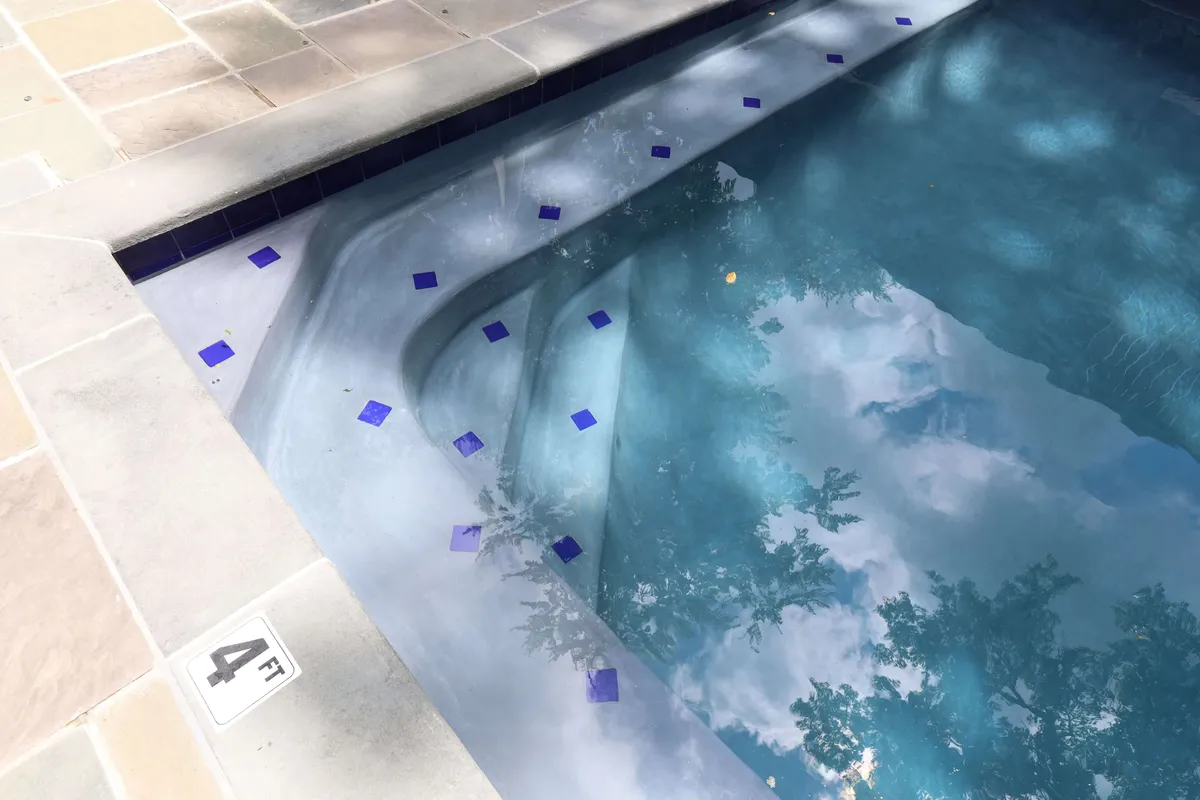 A serene view of the heated saltwater pool, its blue tiles gleaming under natural light. Reflections shimmer on the water’s surface, suggesting both daytime relaxation and tranquil evening swims. The fenced and gated surroundings provide a sense of privacy and exclusivity.