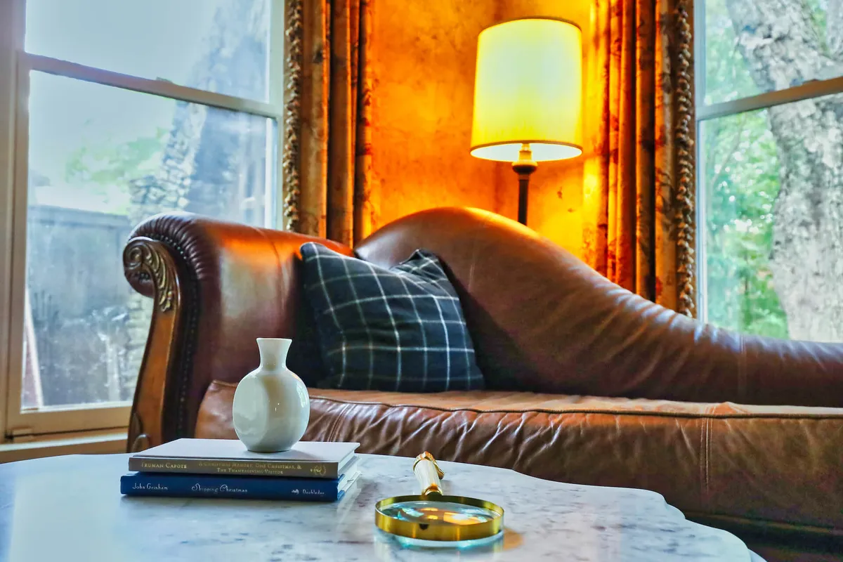 A cozy living room featuring a plush leather sofa, a table with books and a vase, and a softly glowing lamp. The space feels welcoming, ideal for socializing or unwinding after a night out.