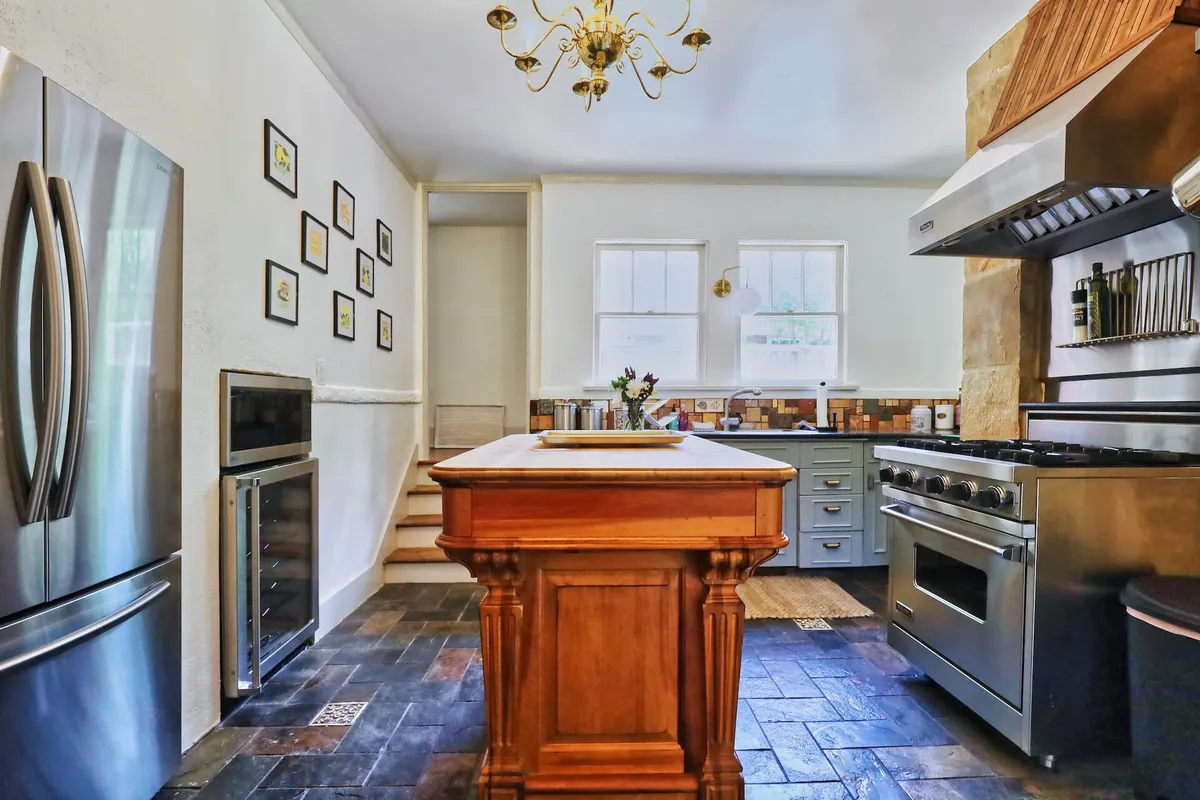 An inviting kitchen view with a prominent wooden kitchen island, sleek stainless steel appliances, and framed pictures adorning the wall. The layout encourages socializing and group cooking, with cozy lighting and practical workspace.