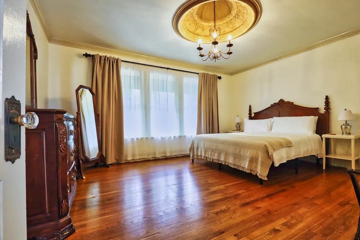 A spacious king bedroom filled with natural light, highlighted by a luxurious bed, elegant chandelier, and tasteful decor. The atmosphere is calm and restful, perfect for recharging after a lively night in the city.