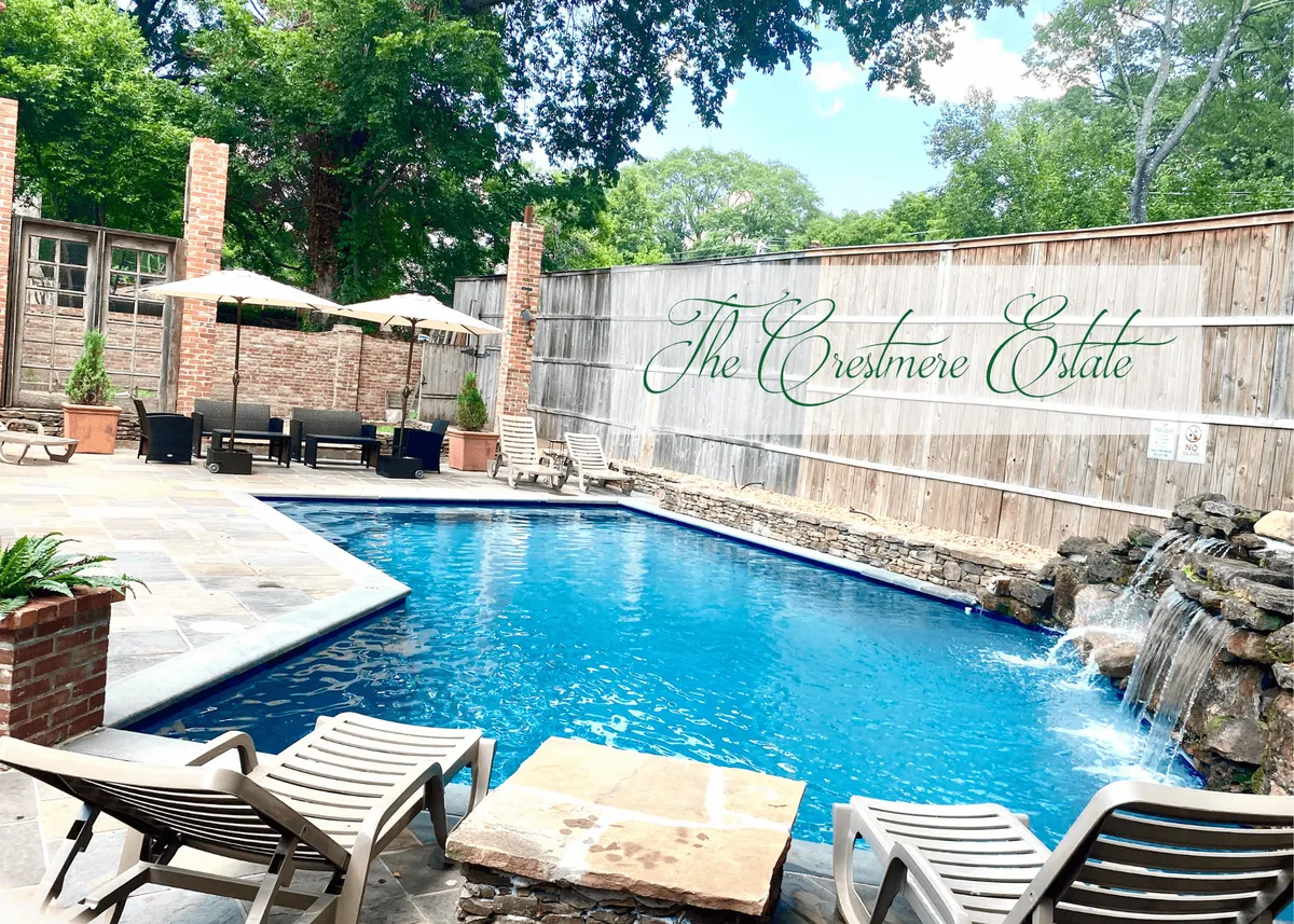 This exterior image features a luxurious swimming pool with a waterfall, surrounded by an inviting outdoor seating area and brick pillars. The space is designed for both relaxation and gatherings, with lush landscaping and plenty of open sky visible.
