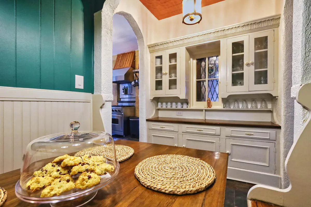 A cozy dining room featuring a wooden dining table adorned with freshly baked cookies, cabinets with glass doors, and woven placemats. The setup suggests an inviting, everyday dining experience that's both comfortable and celebratory.
