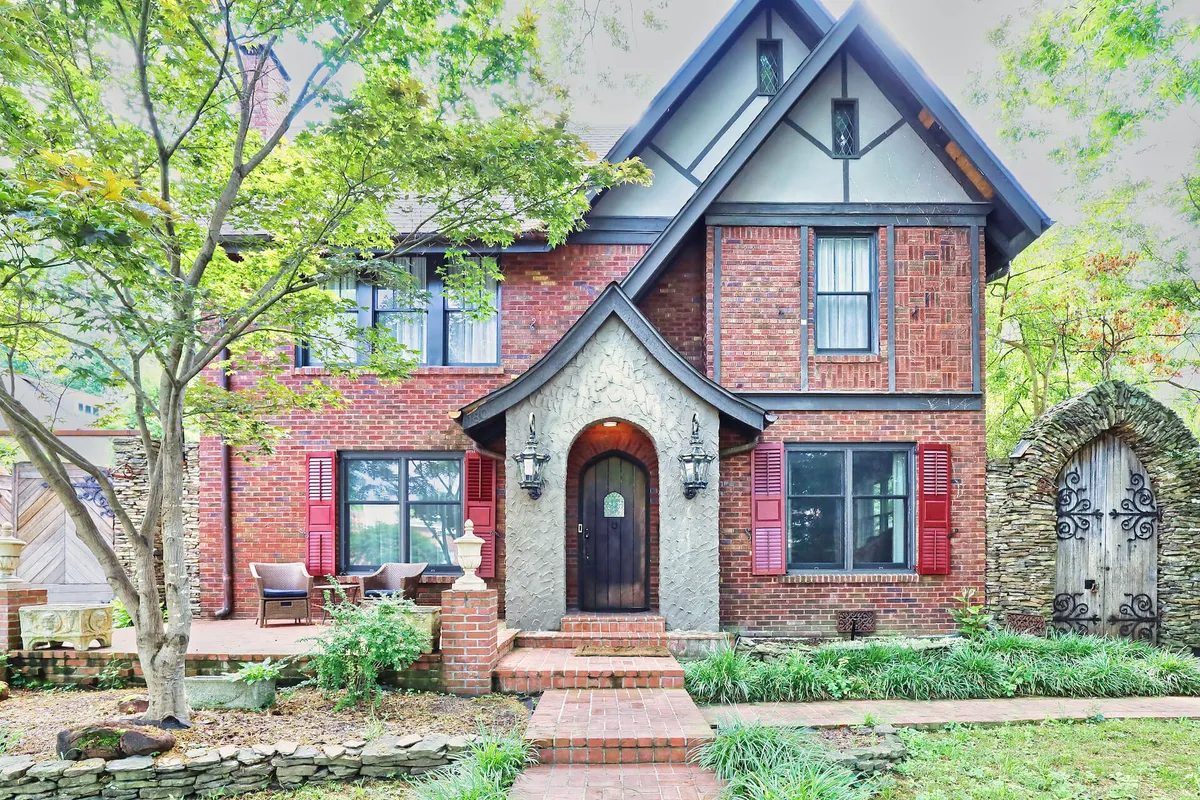 This photo captures the welcoming exterior of the property, featuring an arched doorway, cheerful red shutters, elegant stone detailing, and a beautifully landscaped garden. The scene suggests a vibrant and spacious area perfect for gatherings and outdoor family fun.